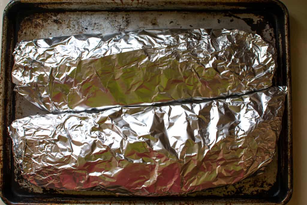 Two racks of ribs wrapped in foil sitting on a baking sheet. 