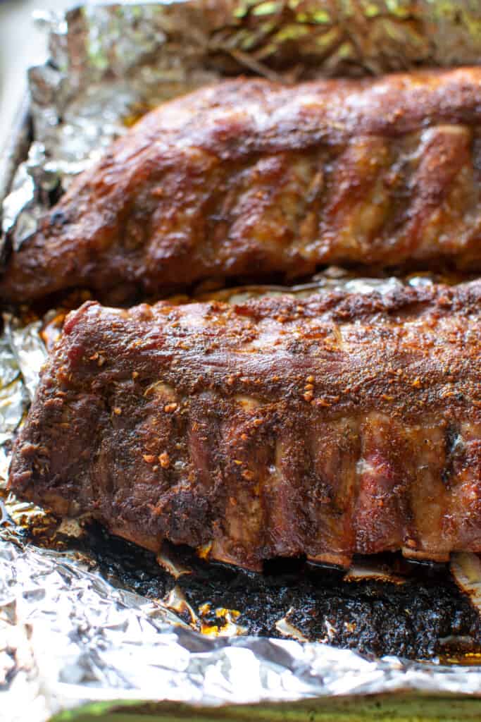 Two racks of baby back ribs sitting on a baking sheet that have been baked. The baking sheet is covered with foil. 