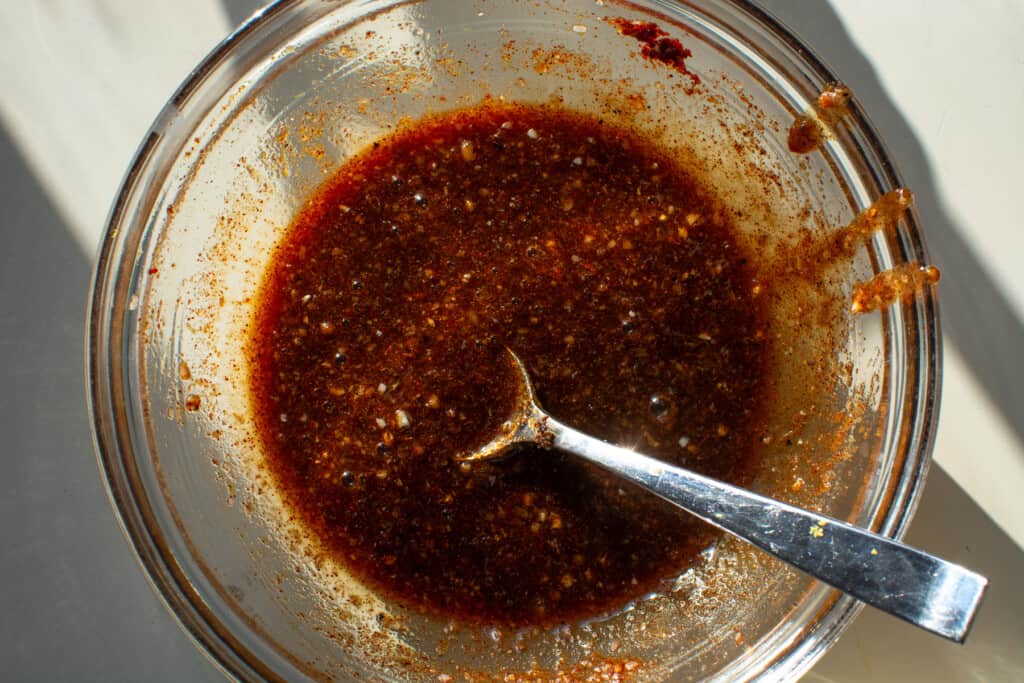 A glass bowl filled with red sauce sitting on a white counter with a spoon in the sauce. 