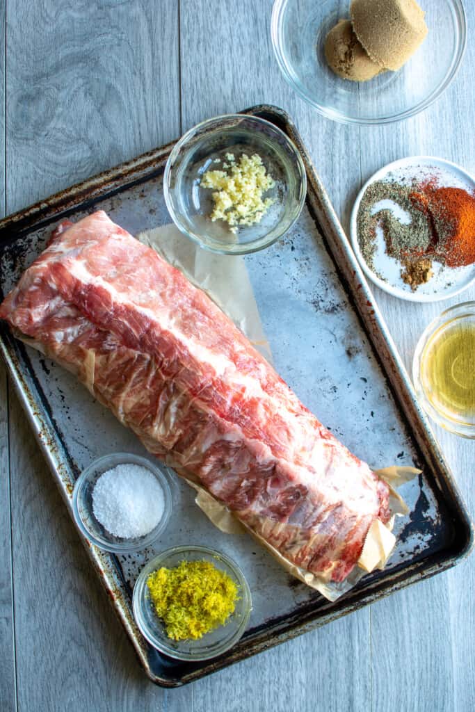 All the ingredients to make baked baby back ribs including pork baby back ribs, lemon zest, garlic, spices, salt, and more. 
