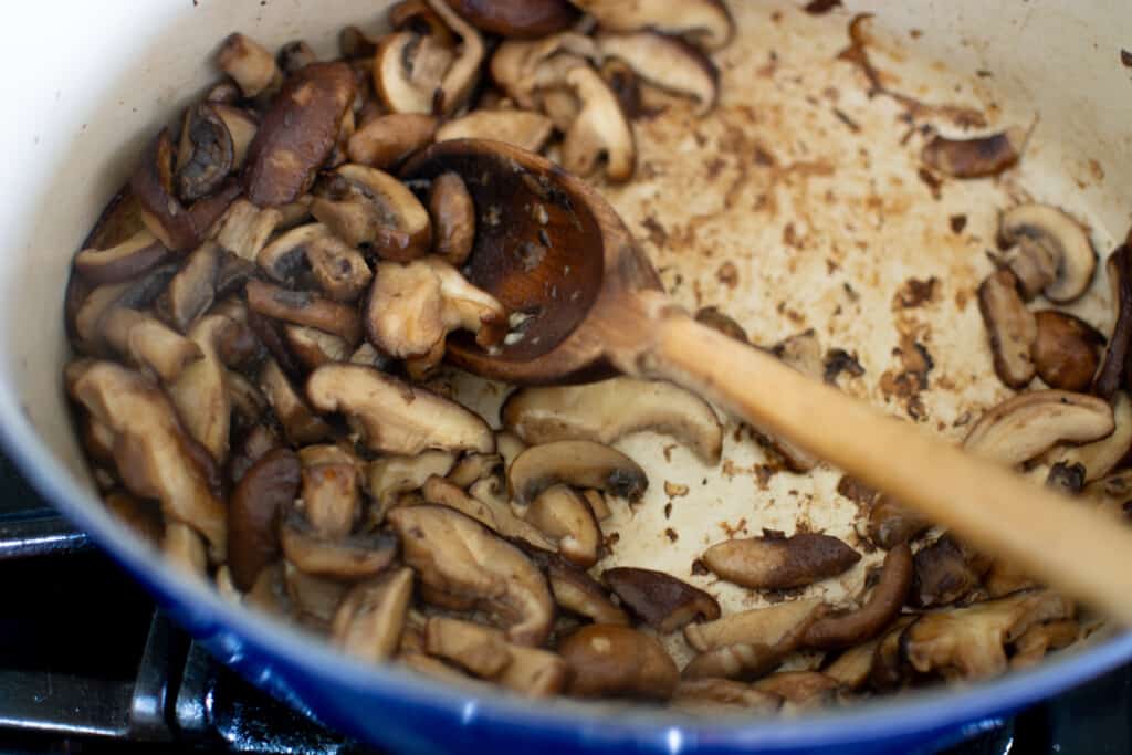 Sliced mushrooms that are being browned in a blue pot. 