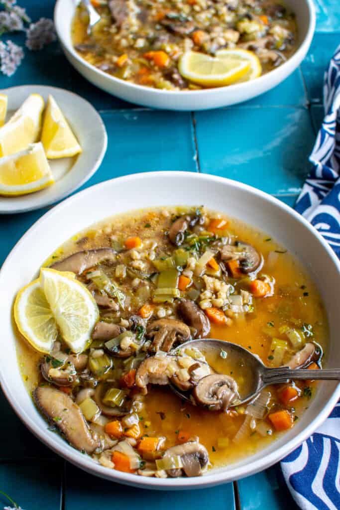 A white bowl of mushroom barley soup with a few slices of lemon on top. 