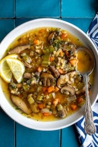 A white bowl of mushroom barley soup with slices of lemon on the side.