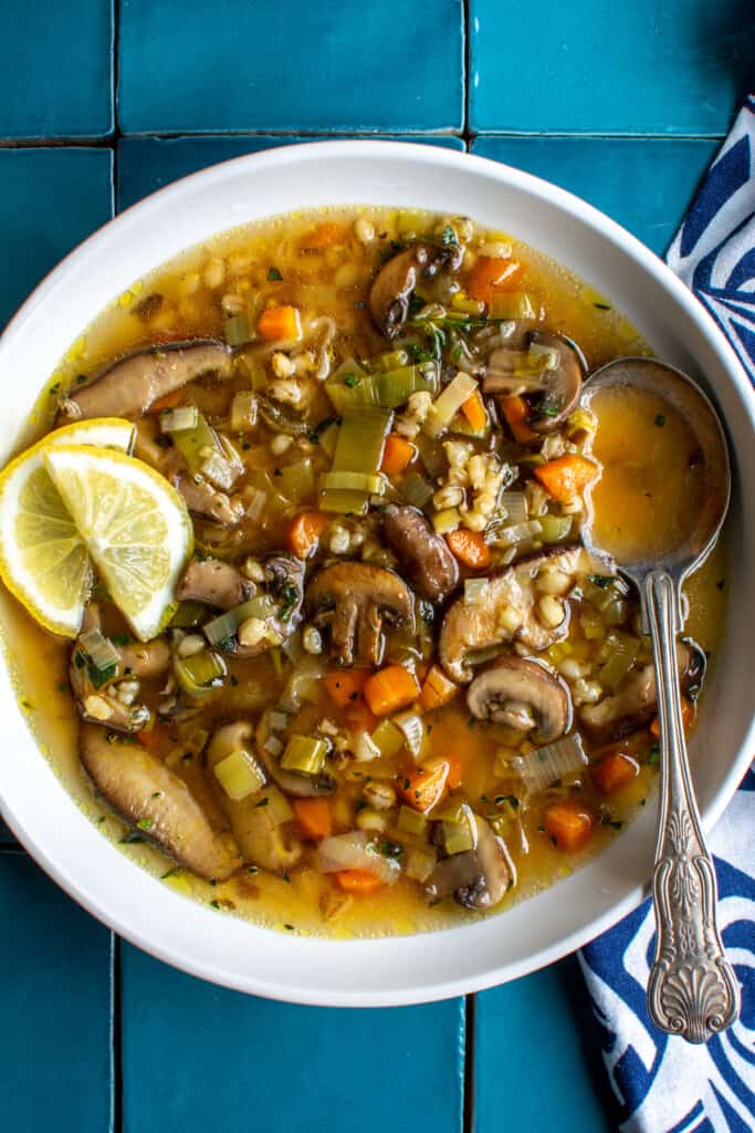 A white bowl of mushroom barley soup with slices of lemon on the side. 