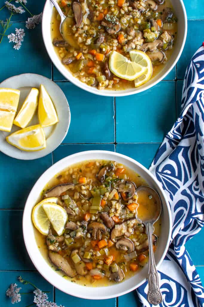 two bowls of barley soup on a blue tile background