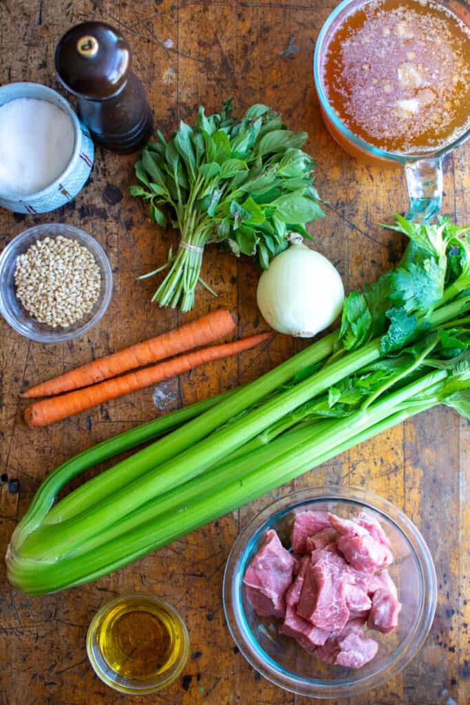 All the ingredients to make beef and barley soup including carrots, celery, beef, broth, fresh herbs, and more