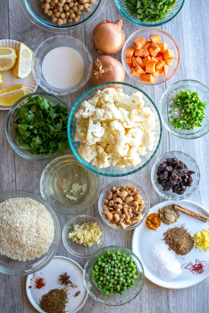 All the ingredients needed to make vegetable biryani including rice, cashews, cauliflower, peas, spices, raisins, and more. 