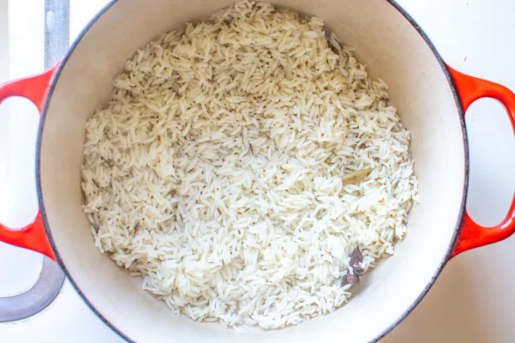 A red pot with cooked rice in the bottom sitting on a white counter. 