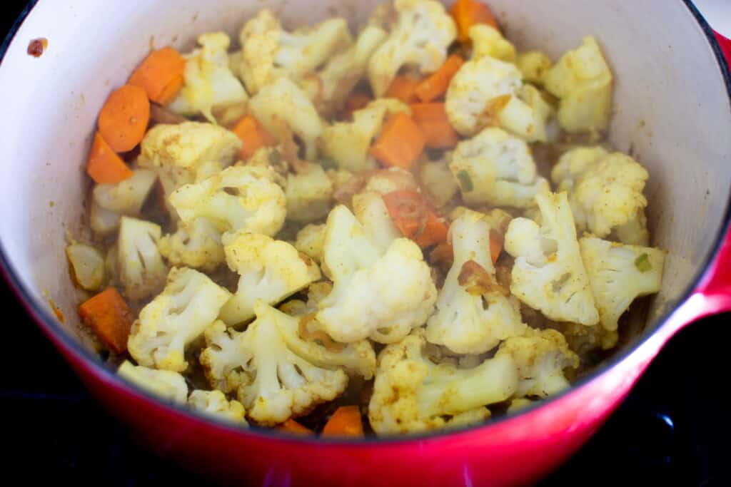 A red pot with cauliflower, chopped sweet potato, chopped jalapenos, and spices. 