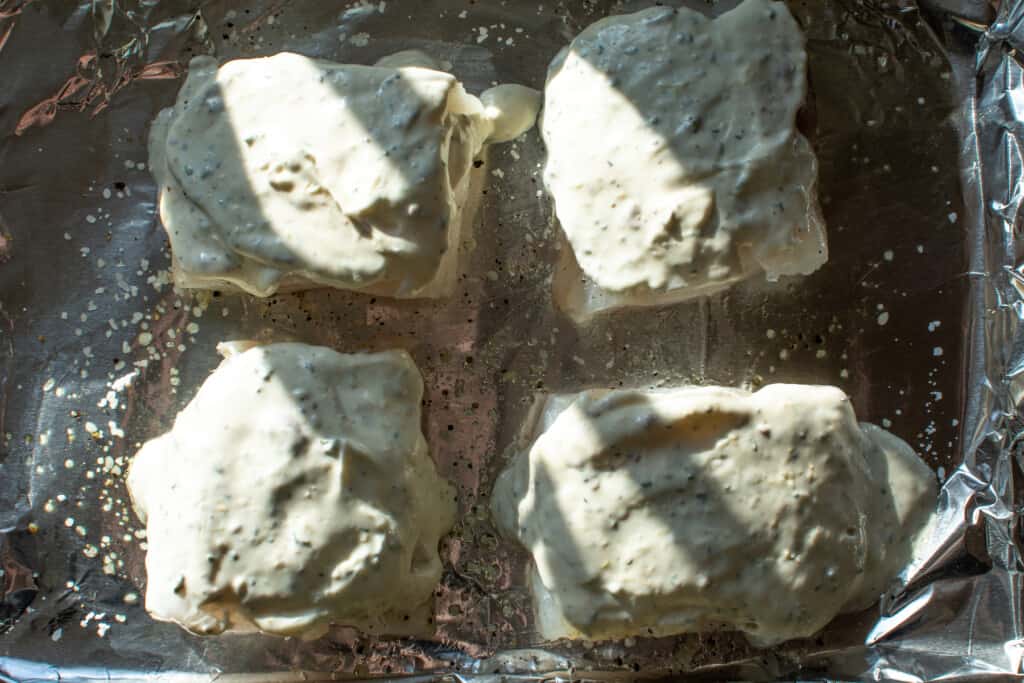 Four pieces of cod coated with the lemon sauce sitting on a baking sheet covered with aluminum foil. 