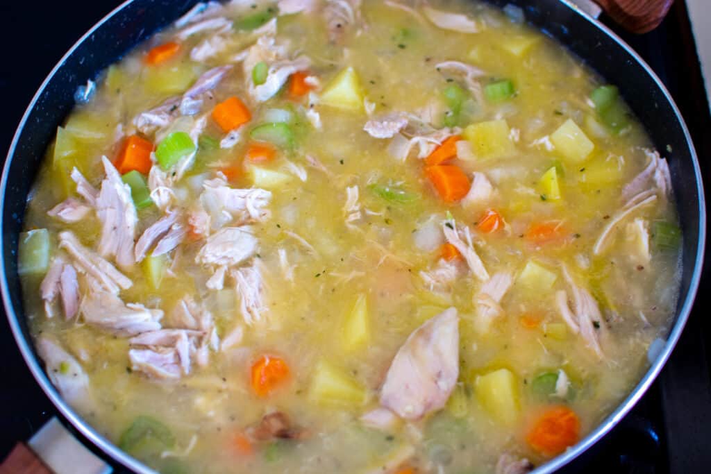 A black pan filled with the filling to make dairy-free chicken pot pie including shredded chicken, vegetables, and more. 