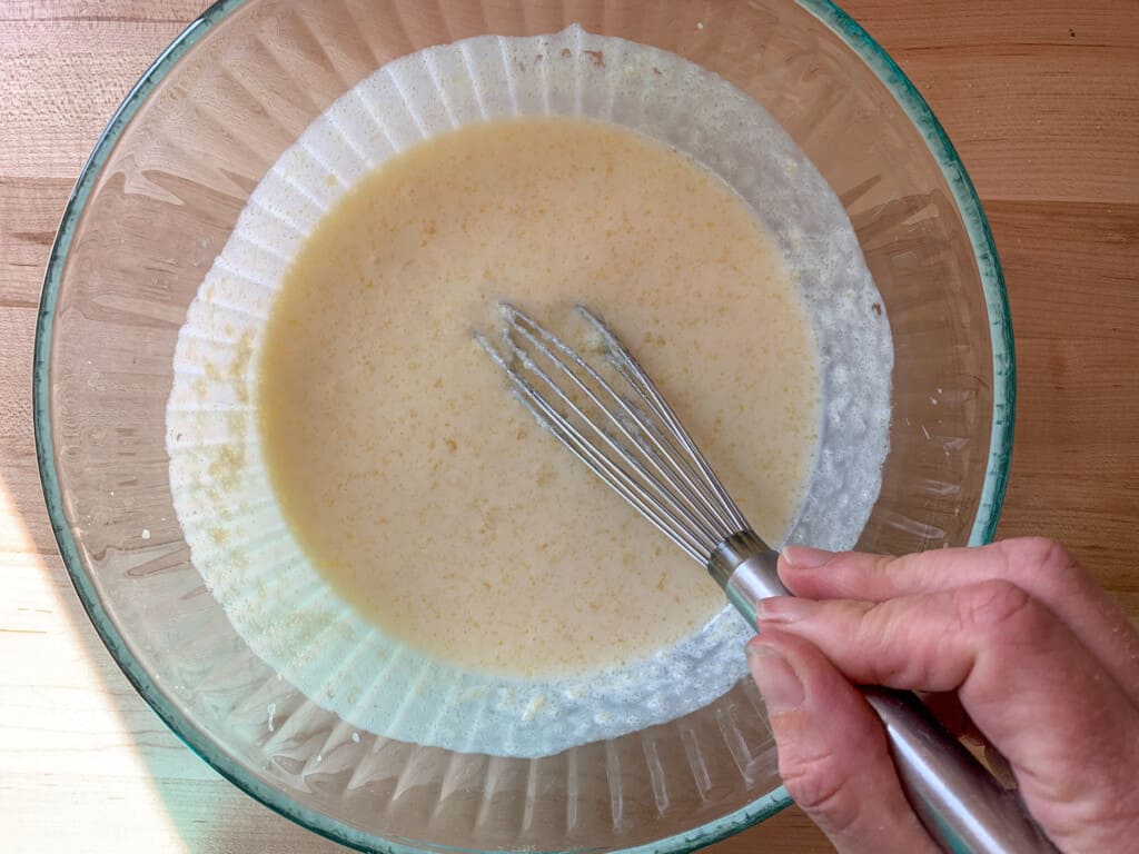 A hand whisking together all the wet ingredients with a whisk. 