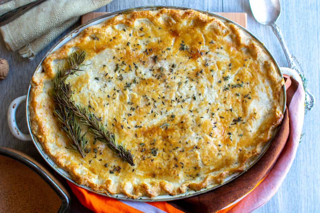 The finished, baked dairy-free chicken pot pie sitting on a wood cutting board on a gray counter top next to a spoon.