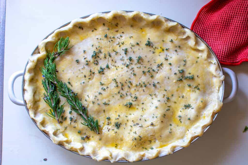 The finished dairy-free chicken pot pie sitting on a white counter ready to go in the oven topped with rosemary sprigs. 