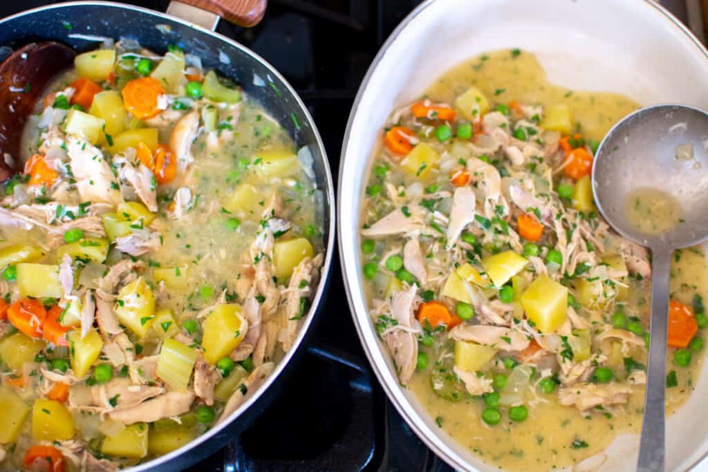 Two pans sitting on the stove. One black one and one white casserole dish with a ladle in it. Both pans have chicken pot pie filling. 