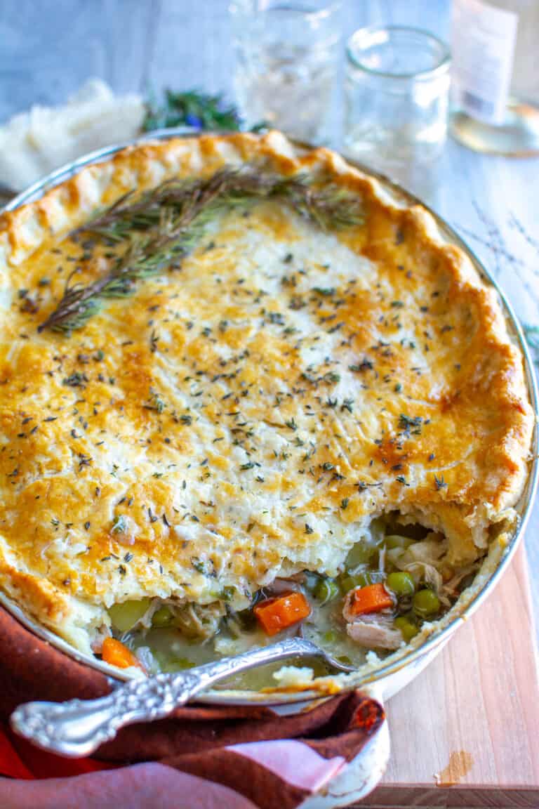 A casserole dish of dairy-free chicken pot pie on a wood cutting board with a spoonful taken out of it and a spoon sitting in the space.
