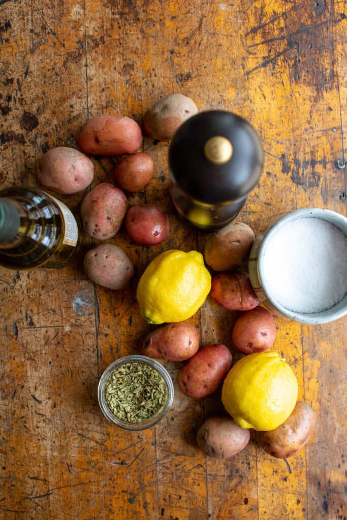 All the ingredients to make roasted baby potatoes including baby potatoes, lemon, oregano, olive oil, salt, and pepper. 