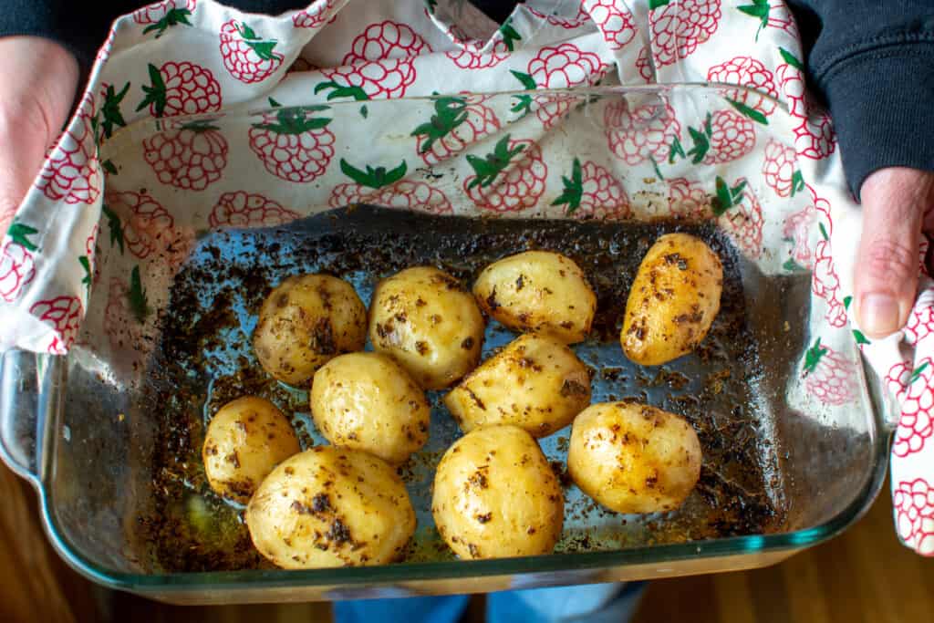 A woman holding a pan of roasted potatoes with a white kitchen towel that has raspberries on it. 