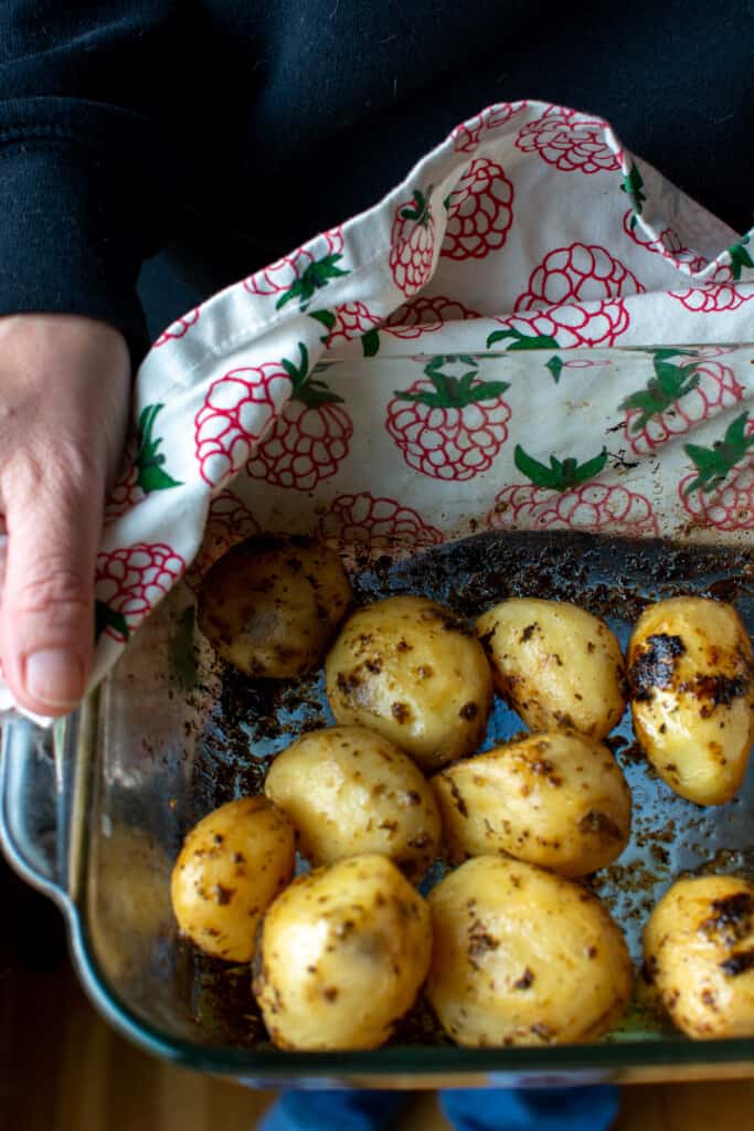 A person holding a baking dish of roasted baby potatoes. 