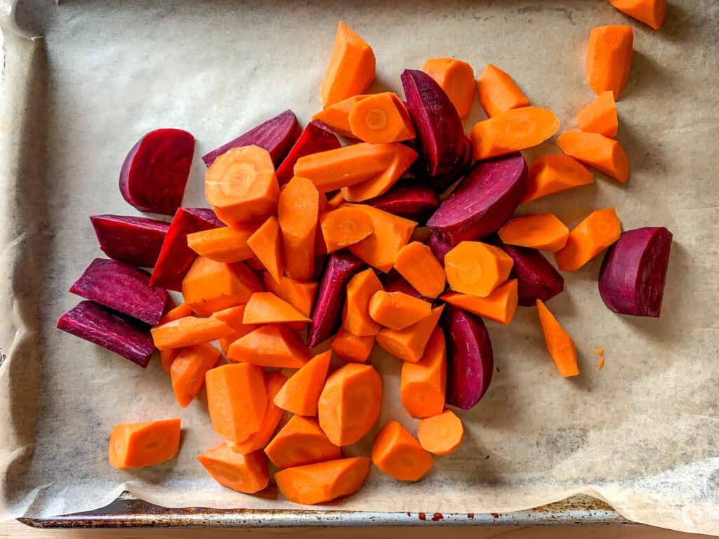 Beets and carrots on a parchment-lined baking sheet. 