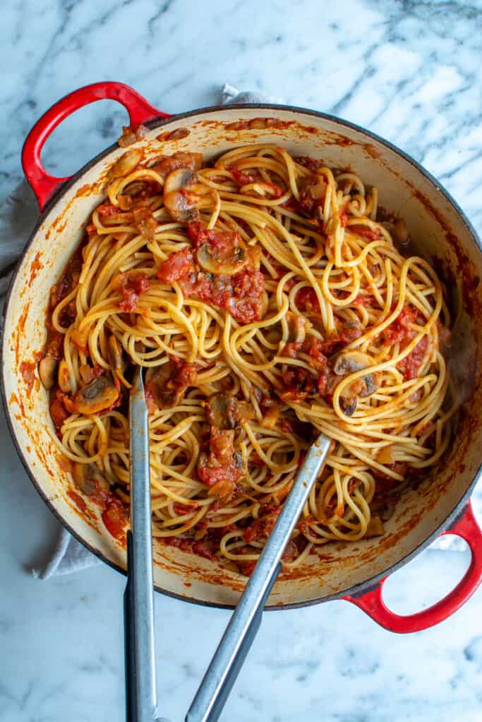 A red pot of mushroom spaghetti sauce with tongs sticking out of it. 