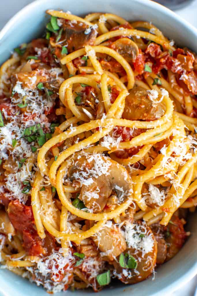 A close up image of pasta with tomato mushroom sauce in a bowl with parmesan on top. 