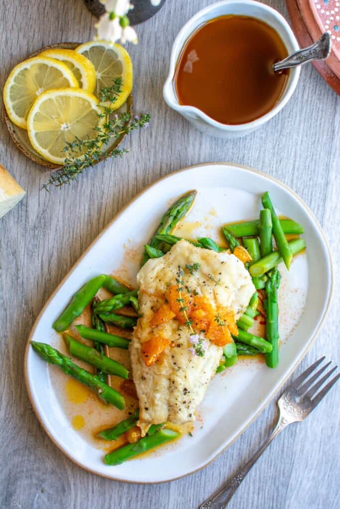 A plate of pan sear fish next to some lemon slices. 