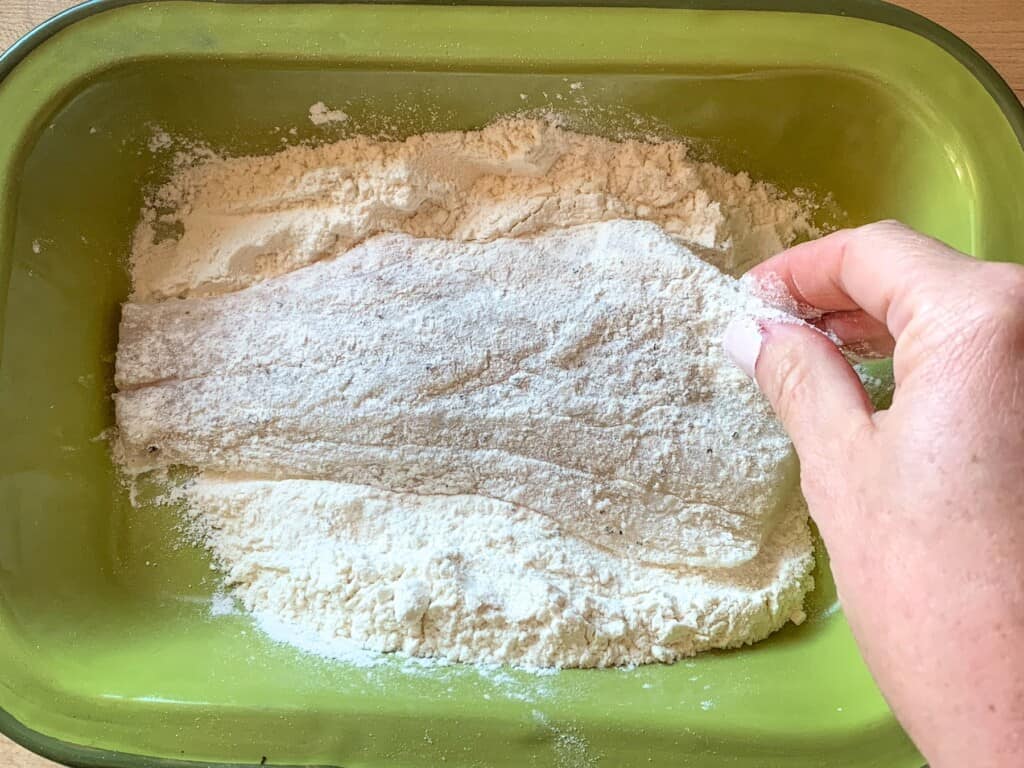 A fillet of fish being dipped in flour. 