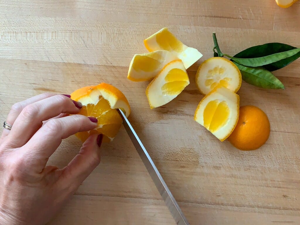 A hand segmenting an orange with a sharp knife. 