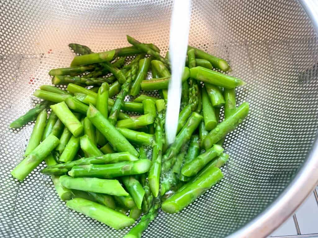 Asparagus in a colander running under cold water