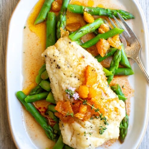 A white plate with asparagus and white fish on it