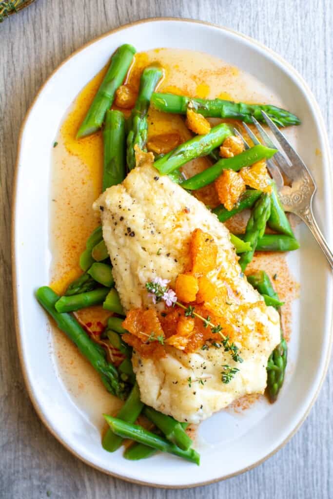 A white plate with asparagus and white fish on it