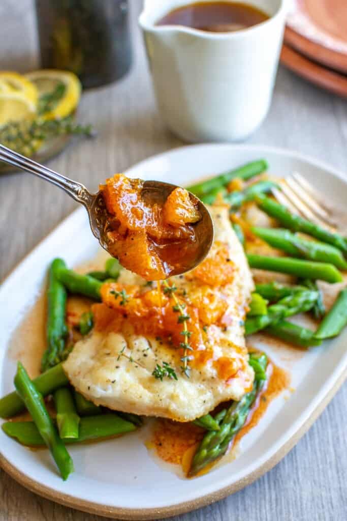 A spoon drizzling orange balsamic dressing over pan sear fish recipe.