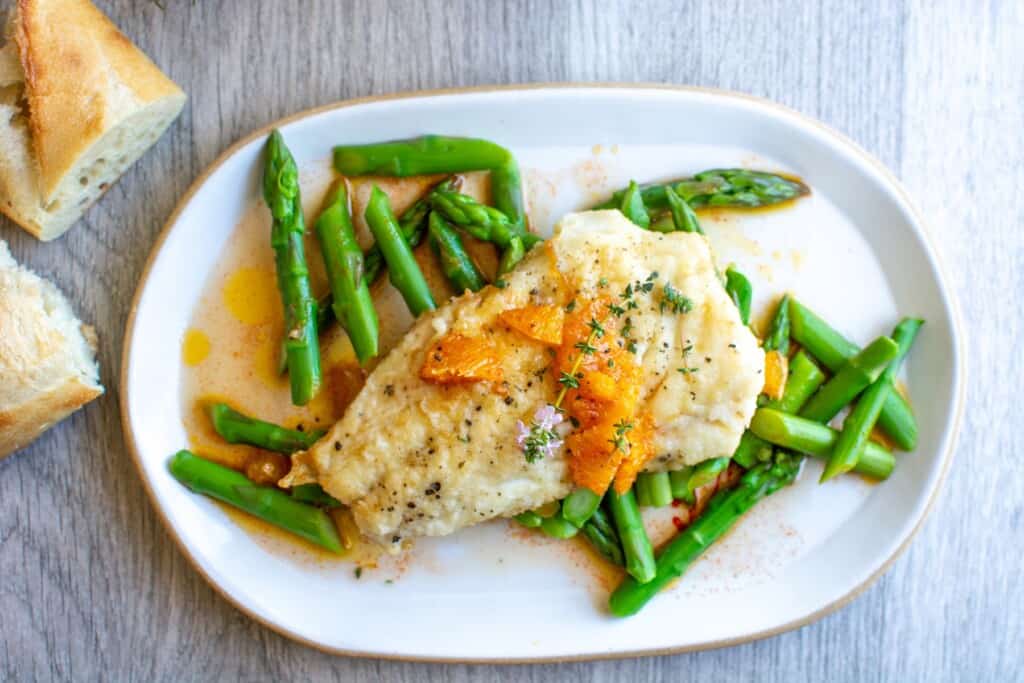 Pan sear fish recipe on a white plate with asparagus underneath. 