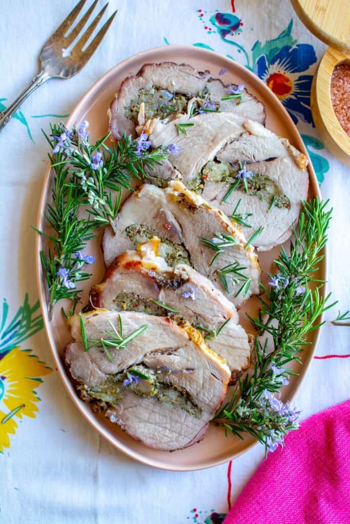 Slices of porchetta roast on a pink plate with a fork next to it. 