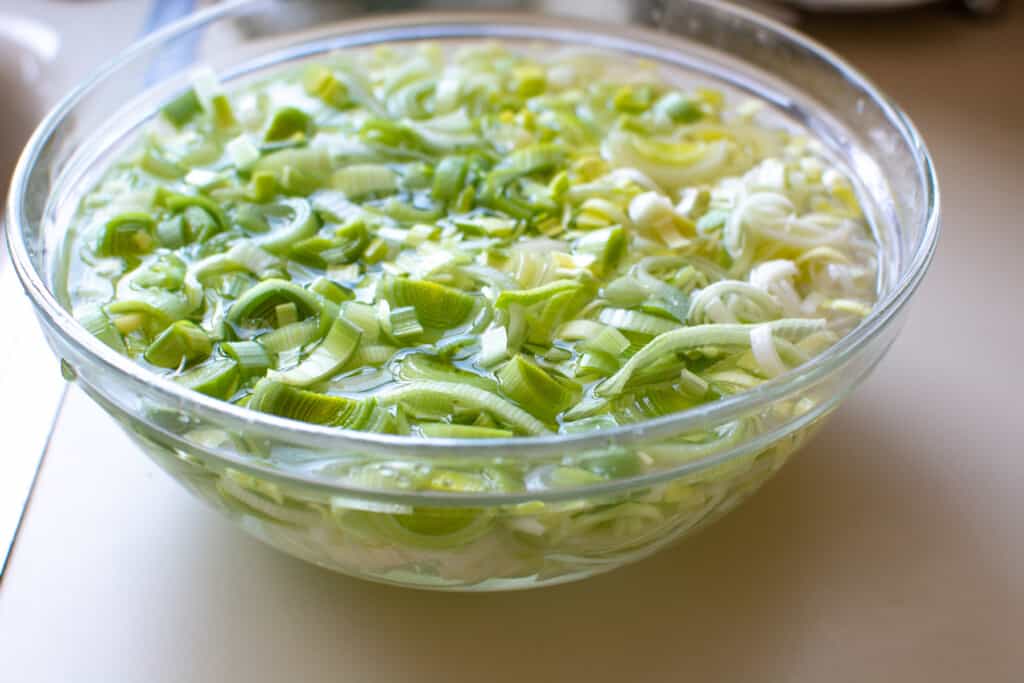 A glass bowl filled with sliced leeks that are soaking in water sitting on a white counter. 