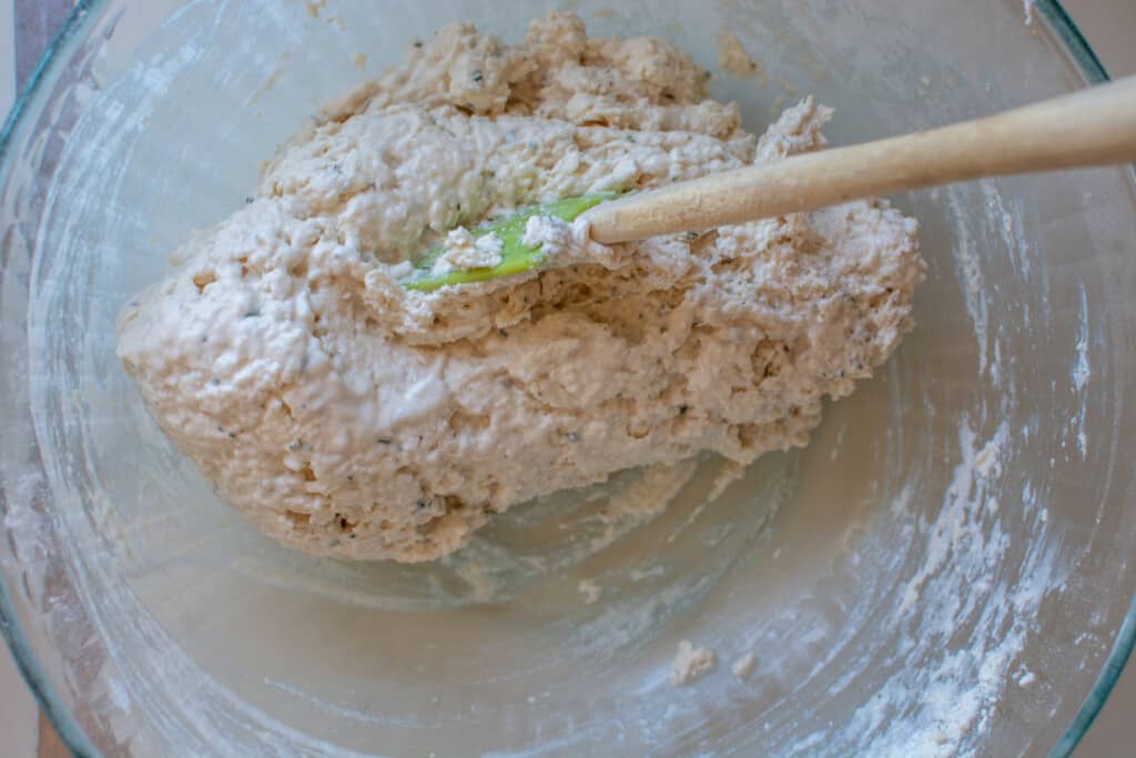 Biscuit dough being stirred in a glass bowl by a rubber spatula. 