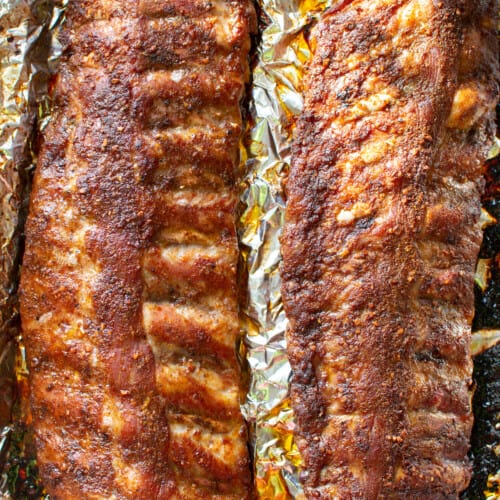 Two racks of ribs sitting on a foil-lined baking sheet after being baked.