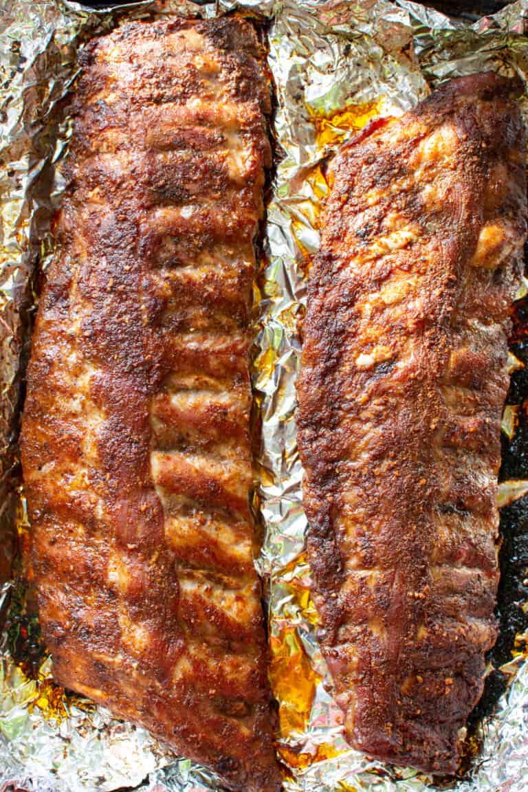 Two racks of ribs sitting on a foil-lined baking sheet after being baked.