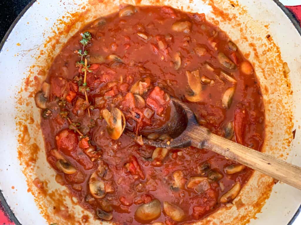 A wood spoon stirring tomato mushroom sauce in a big pot on the stove. 