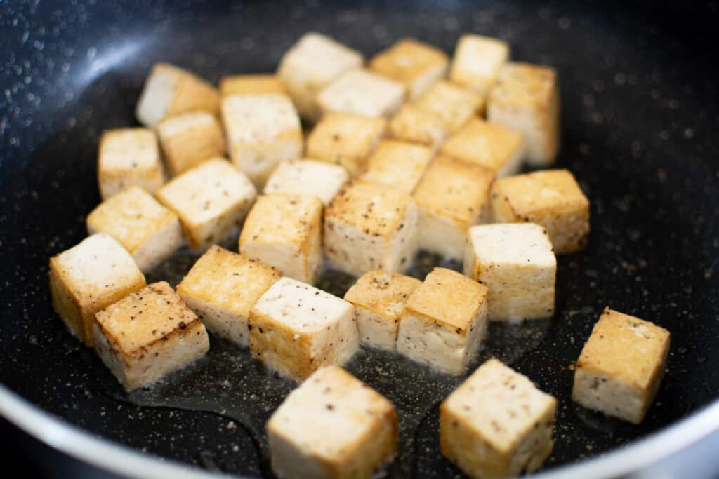 Several blocks of tofu browning in a pan. 