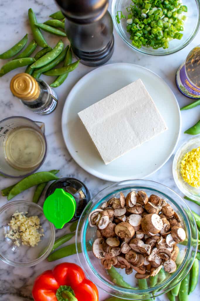 A block of tofu on a plate surrounded by prepped ingredients. 