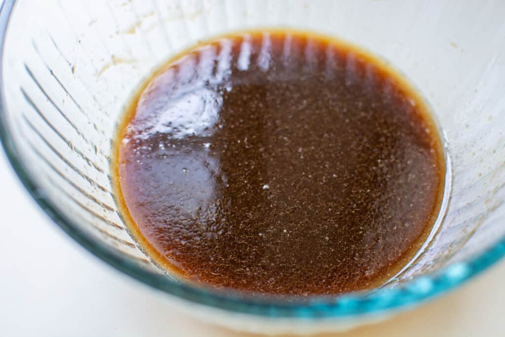 A glass bowl with hoisin sauce in it sitting on a white counter. 