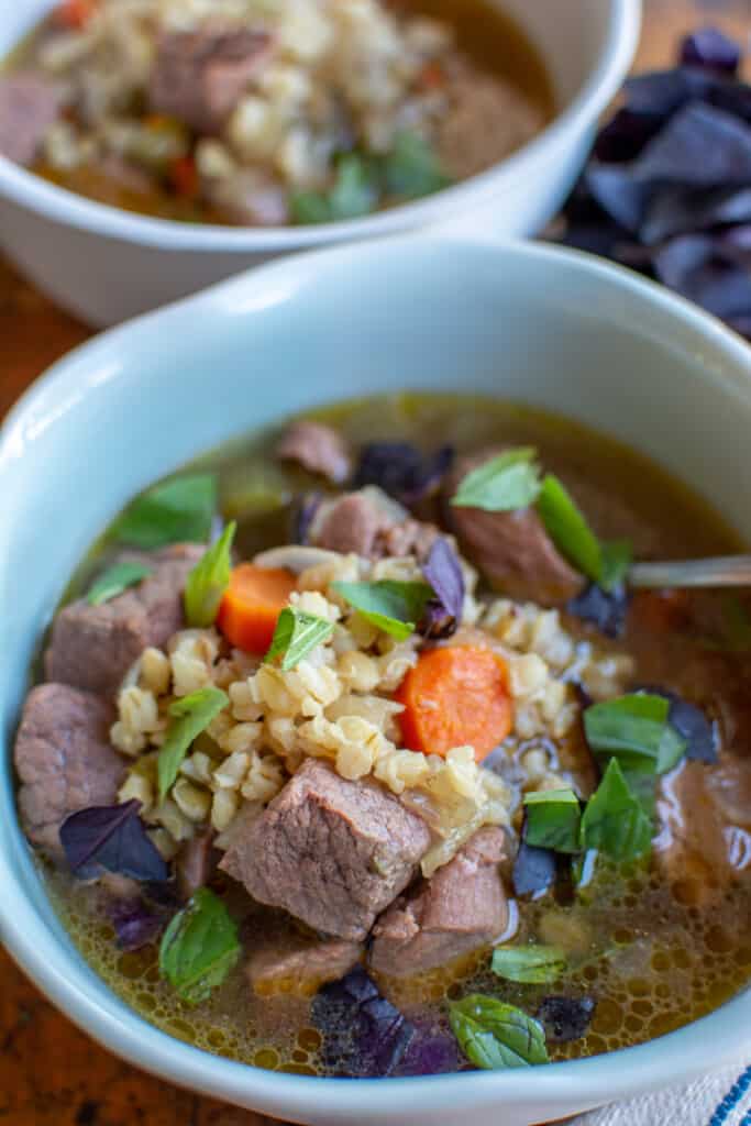 Two bowls filled with beef and barley soup with hunks of beef, carrots, barley, and fresh herbs