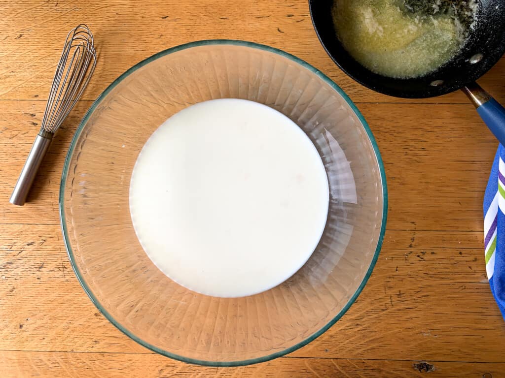 A glass bowl with milk in it on a wood table. 