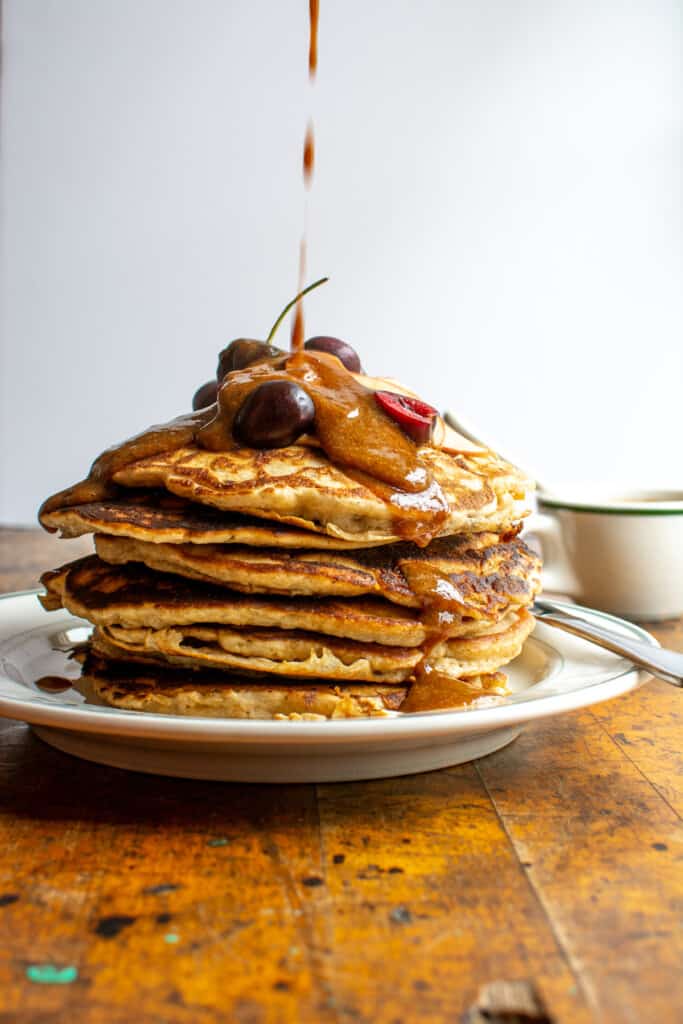 A tall stack of pancakes with syrup being drizzled over them. 