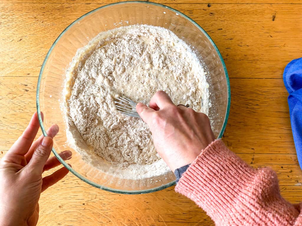 A hand mixing flour and milk in a glass bowl. 
