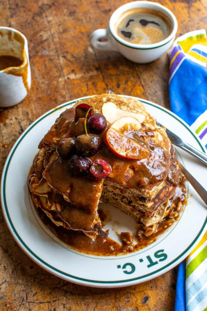 A tall stack of pancakes with fruit on top and a wedge cut out of them. 