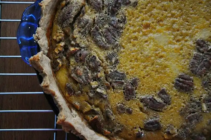 A pumpkin pie with pecans in it in a blue pie plate on a wire rack. 