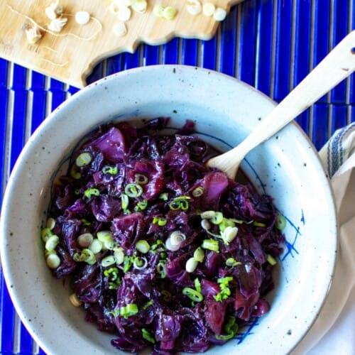 German sweet and sour braised cabbage recipe in a bowl on a blue table.